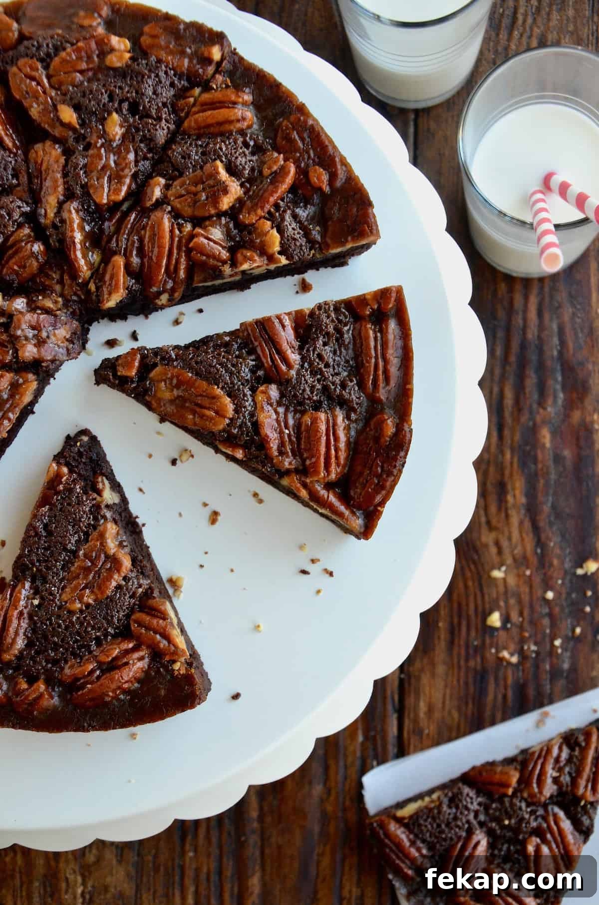 Fudgy Chocolate Brownies Recipe 7 Slices of Pecan Pie Brownies sit on a white scalloped cake stand. Nearby is a glass of milk with two striped straws.