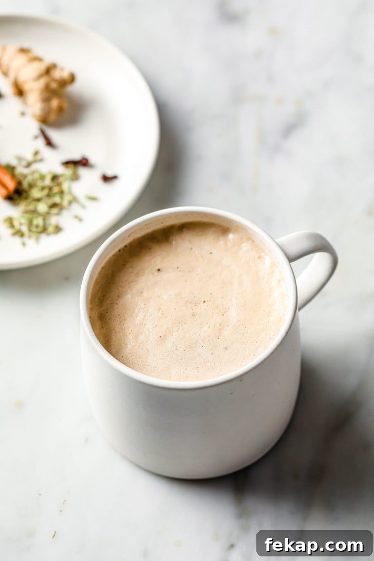 Authentic Masala Chai Recipe: Aromatic Spiced Tea 7 Frothy Chai Tea in a white cup with spices in a plate nearby.
