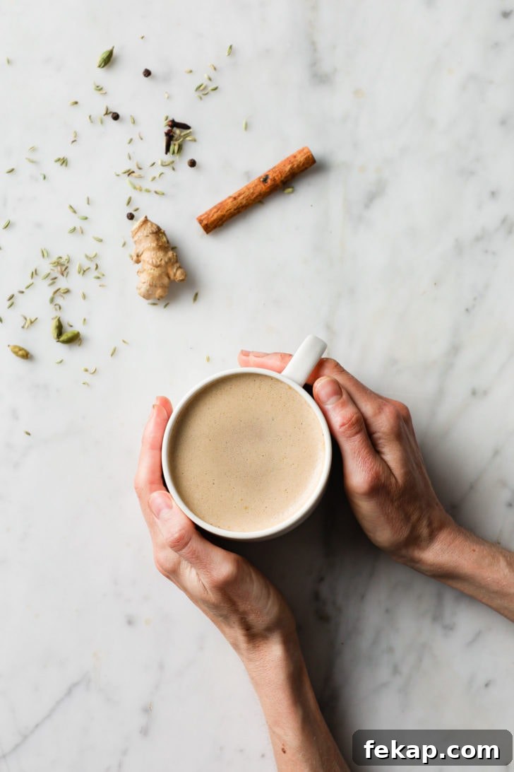 Authentic Masala Chai Recipe: Aromatic Spiced Tea 9 Holding chai tea on a marbled surface with ginger, cardamom, cloves, black pepper, and fennel on the side