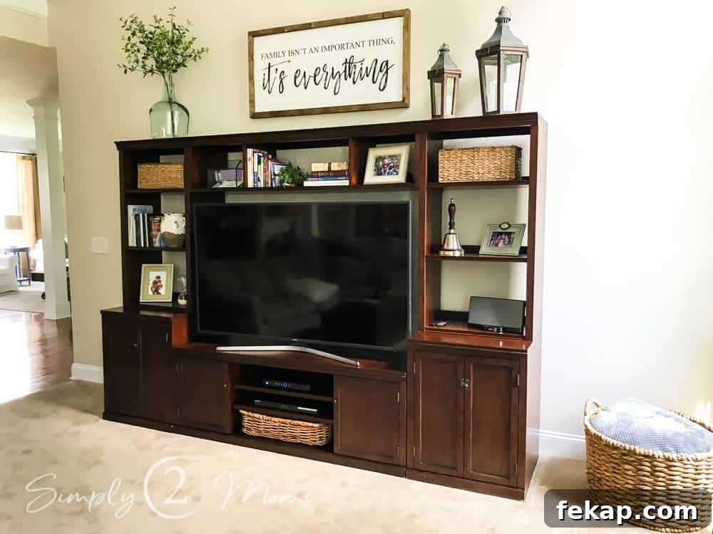 dark wood media unit with flat screen tv. with basket filled with blankets on side. sign, lanterns and vase filled with greenery on top of media center