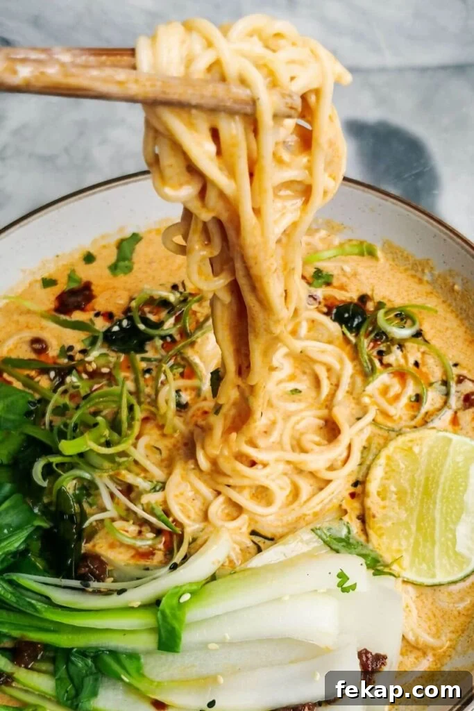 Green Goddess Soba Noodle Salad with Creamy Avocado Dressing 12 Chopsticks pulling up saucy coconut noodles in a white bowl.