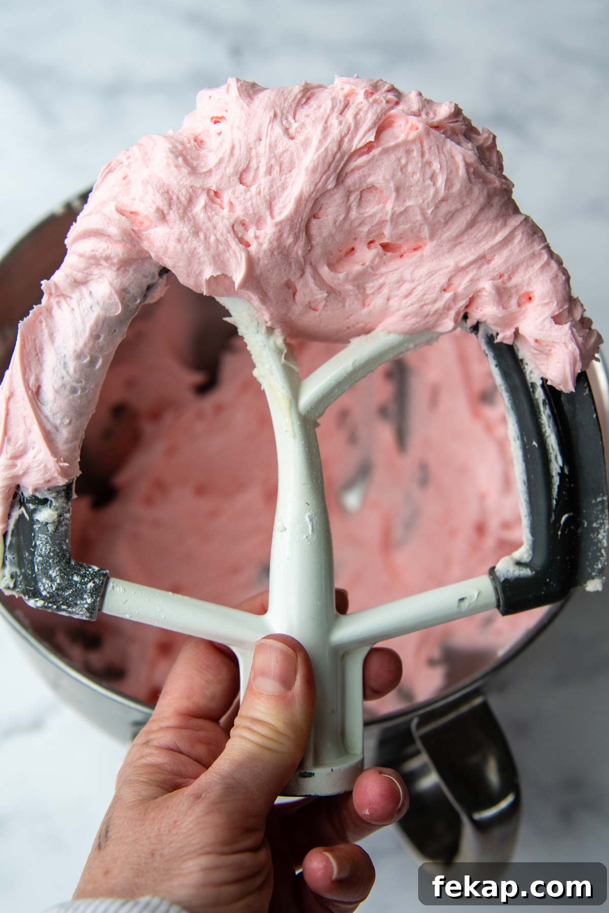 a beater holding up fluffy pink frosting.