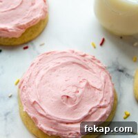 a pink sugar cookie on a white background with sprinkles around and a glass of milk.