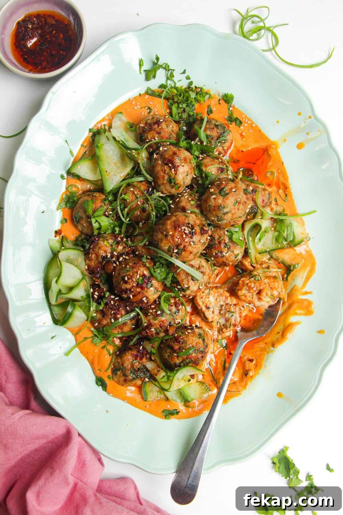 Dumpling meatballs on gochujang sauce with pickled cucumber on an oval platter.