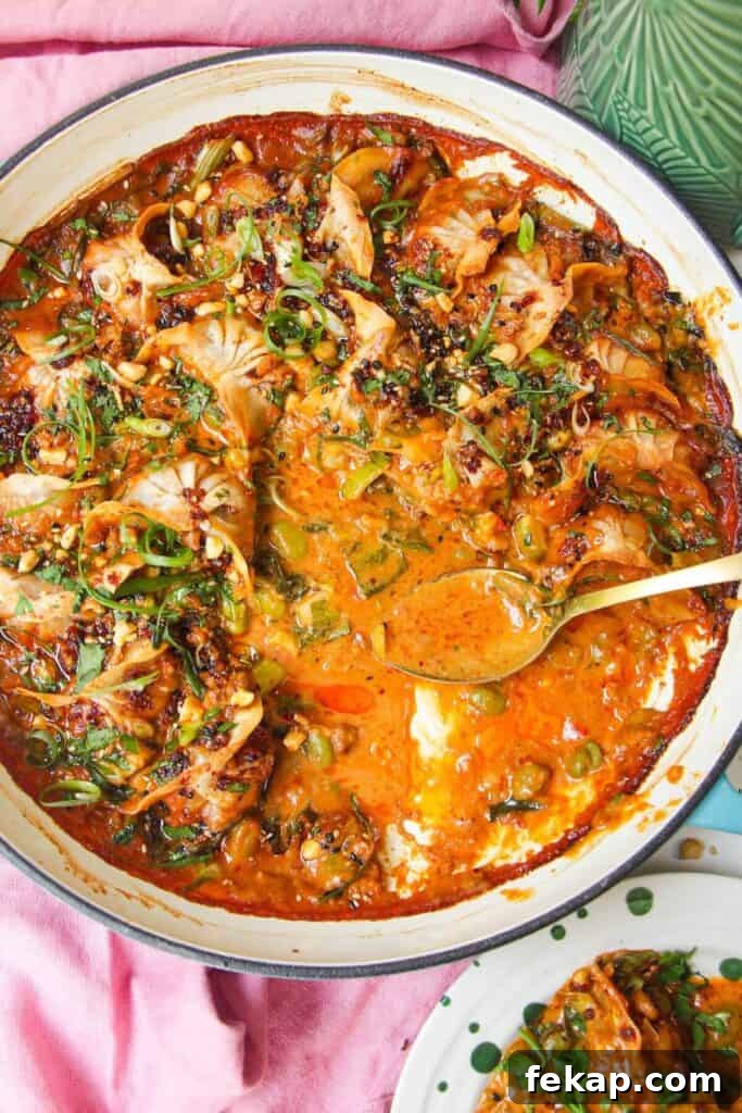 Baked dumplings in satay sauce in a skillet with chili oil on top.