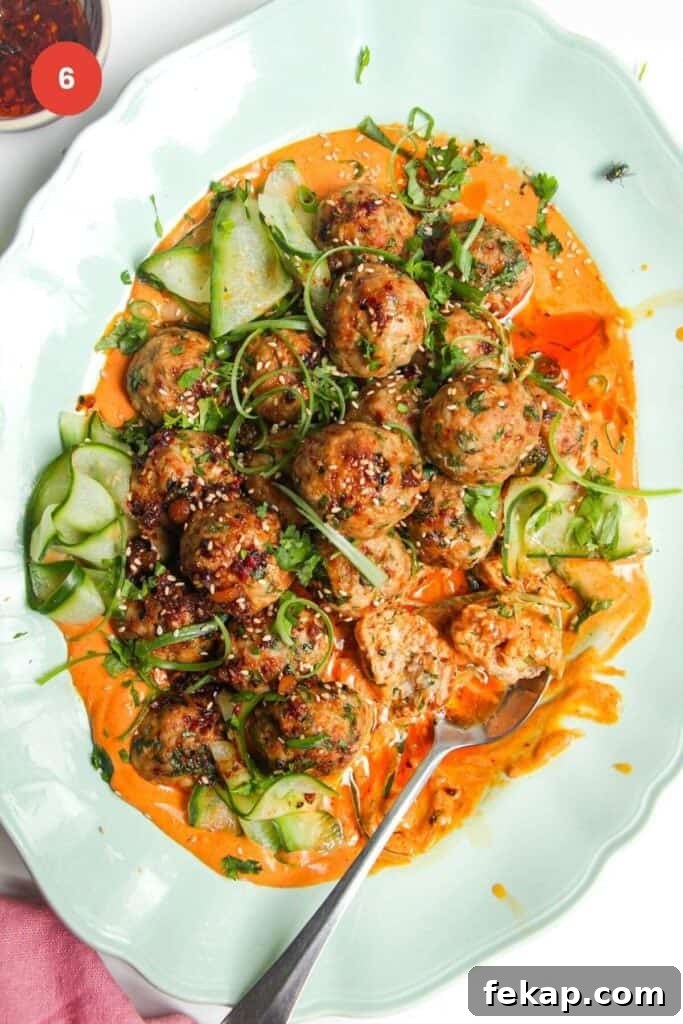 Dumpling meatballs on gochujang sauce with pickled cucumber on an oval platter.