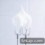 Two beaters with fluffy white frosting holding a stiff peak in front of a gray background.