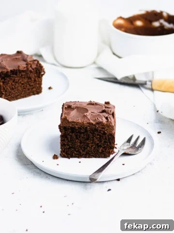 Close up of a square slice of chocolate coffee cake with dark chocolate frosting on a white plate.