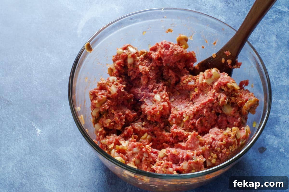 Old-Fashioned Gluten-Free, Dairy-Free Meatloaf (No Eggs or Milk) 6 meatloaf ingredients in a large glass mixing bowl with a wooden spoon in bowl
