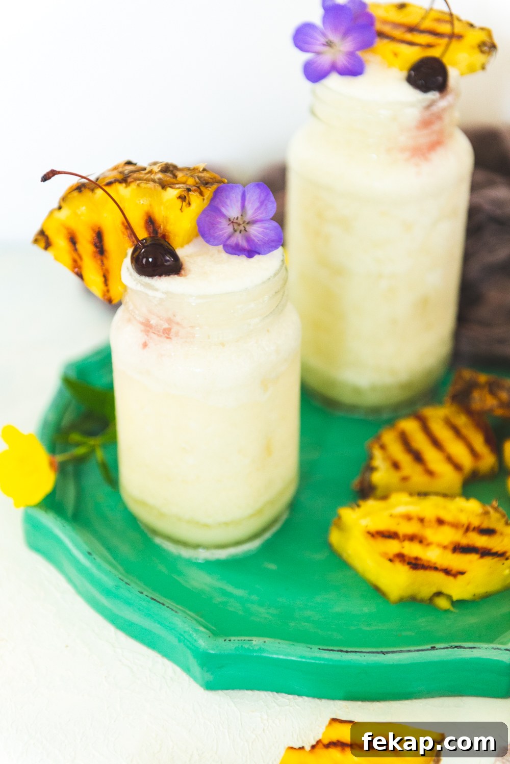 How to Make a Classic Frozen Piña Colada 4 Frozen pina colada cocktails in mason jars garnished with grilled pineapple, cherries and edible flowers.
