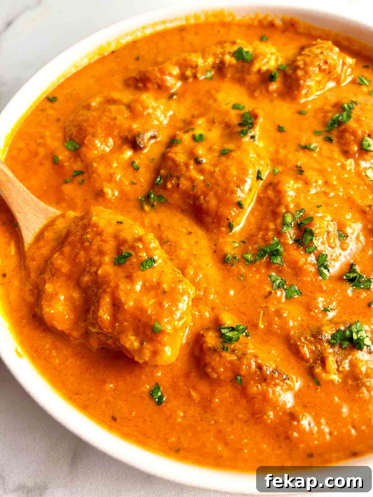 Creamy Butter Chicken Recipe: Authentic Indian Flavor 10 spoon lifting chicken from bowl of butter chicken.