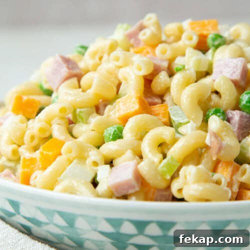 macaroni salad with ham, peas, and cheddar in a blue and white bowl.