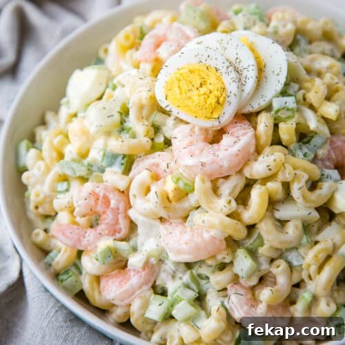 macaroni salad with shrimp topped with hard boiled eggs in a white bowl.