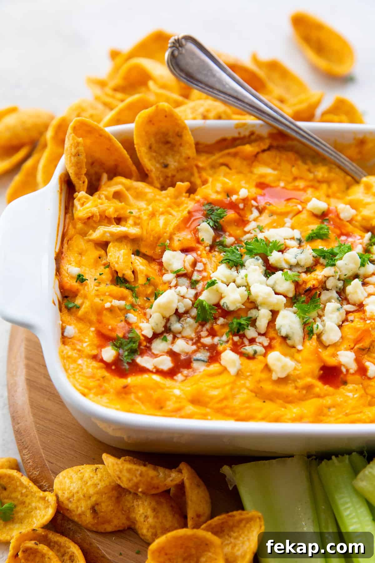 Buffalo Chicken Dip with crumbled blue cheese and buffalo sauce in a white baking dish with a spoon.