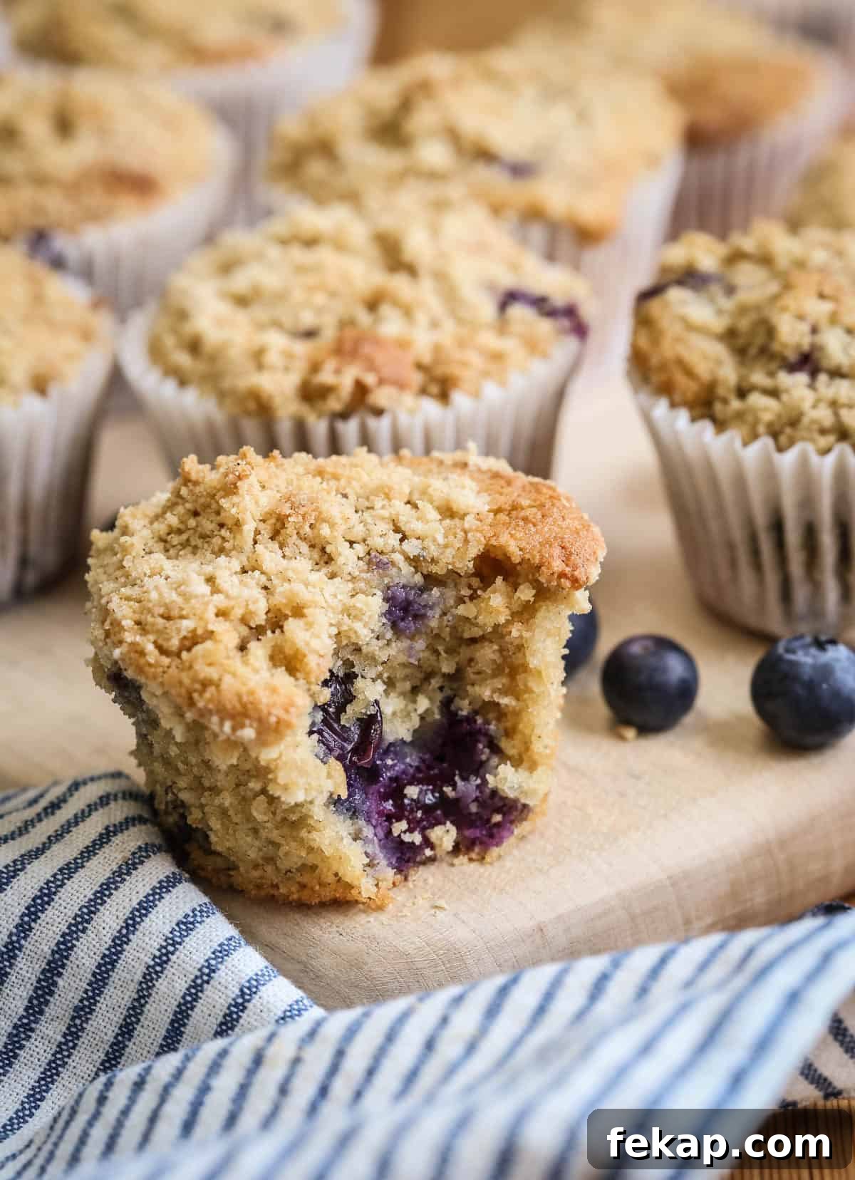 Gluten Free Blueberry Streusel Muffins Recipe 11 Blueberry Muffin on a table with a bite taken out showing juicy blueberries and soft fluffy crumb.