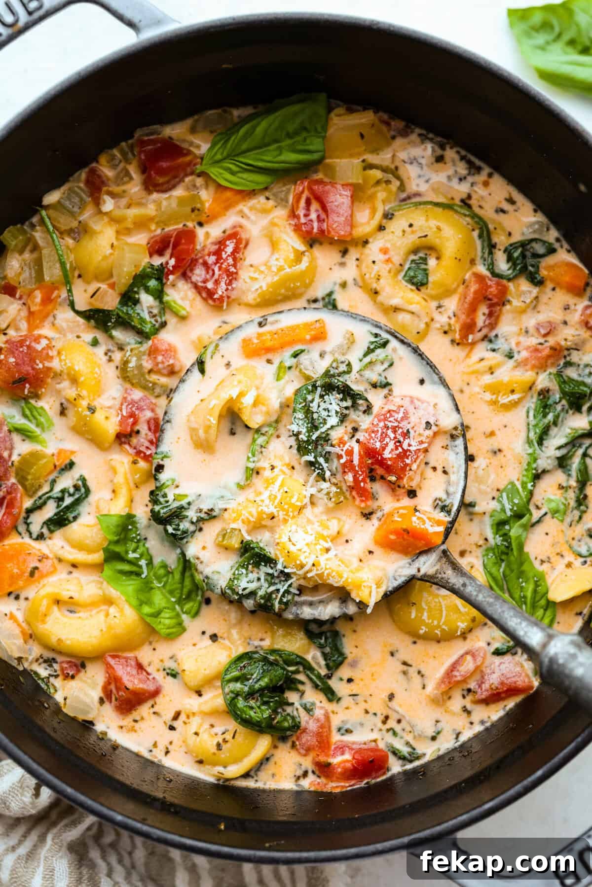 Pot of creamy vegetable tortellini soup with a silver ladle.
