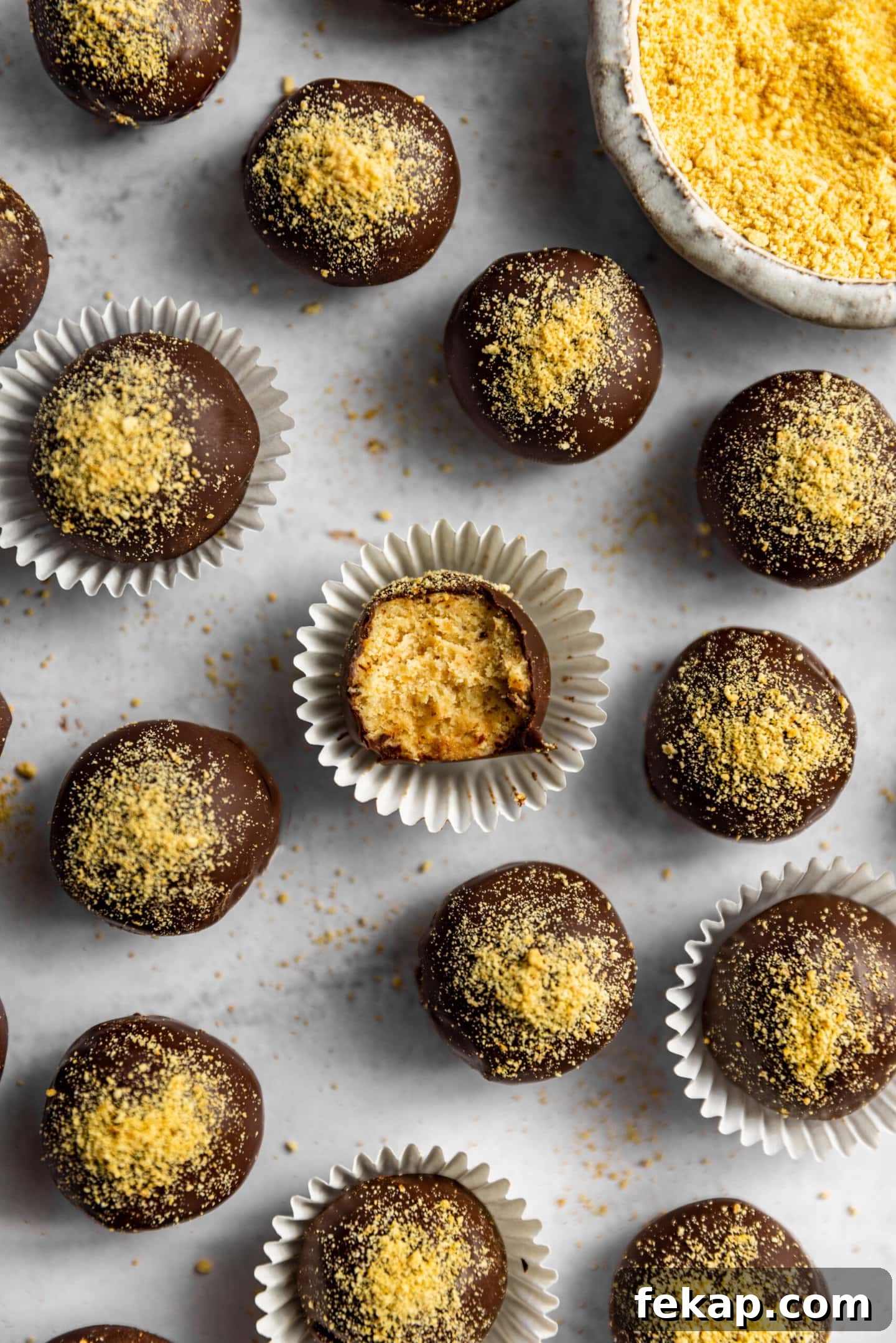 No-Bake Cheesecake Balls next to a bowl of graham cracker crumbs. A bite is missing from one showing the creamy filling.