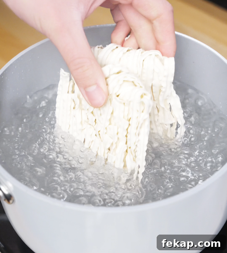 Spicy Chili Garlic Butter Noodles Recipe 4 A hand dropping a block of instant noodles into a pot of rapidly boiling water, marking the start of the noodle prep for chili garlic butter noodles.