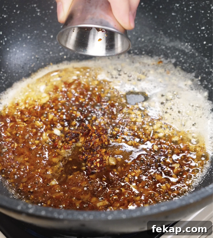 Spicy Chili Garlic Butter Noodles Recipe 6 Soy sauce and chili oil being added to the pan, blending with the garlic butter to create a spicy, umami-rich base.