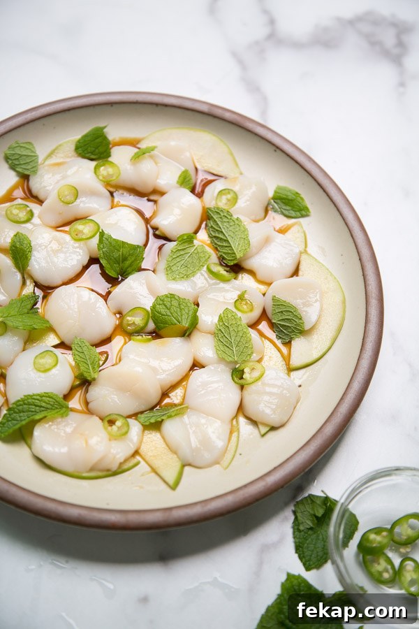 side view of raw scallop crudo on a plate with peppers apples and mint