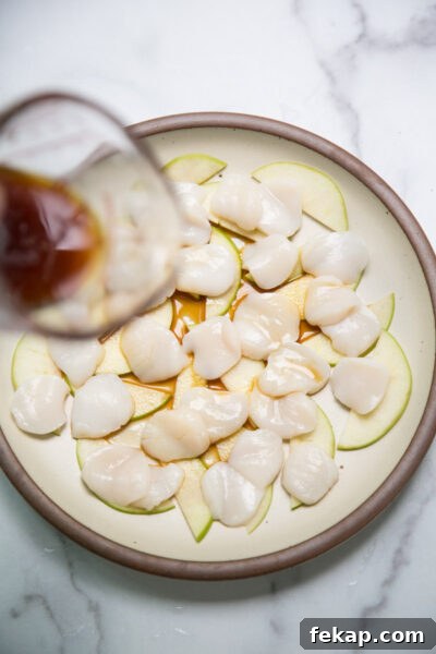 raw scallop crudo on a plate with cut of japanese ponzu sauce pouring over top