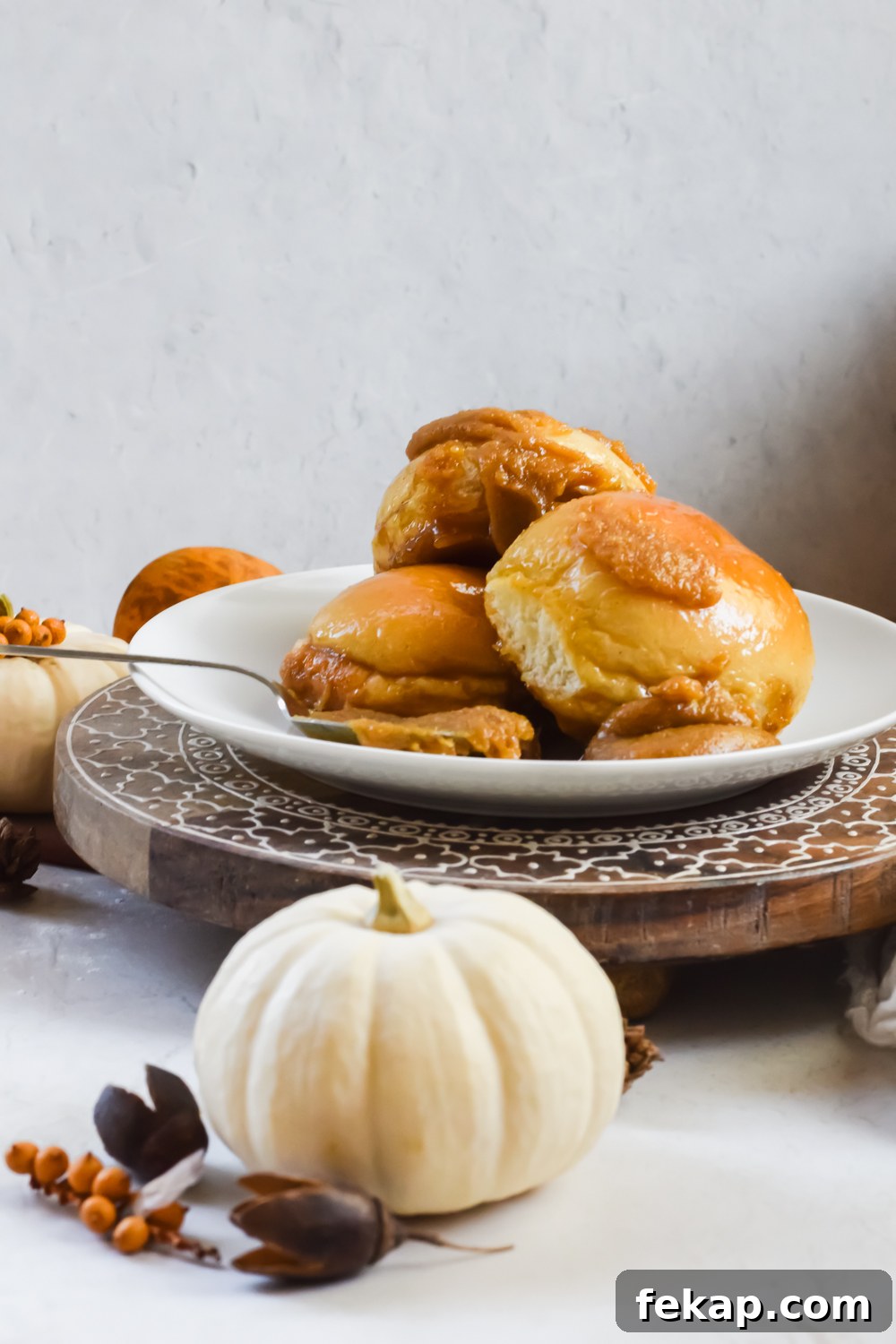 Classic Sticky Buns with Caramel Glaze 8 three baked old fashioned sticky buns stacked on top of eachother on white plate with extra caramel sauce added with pumpkin decoration surrounding.