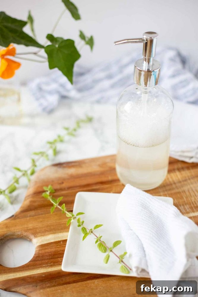 DIY Natural Dish Soap Recipe That Cuts Grease 5 wood cutting board with a white plate and a rag on top and natural dish soap in a glass bottle in the back