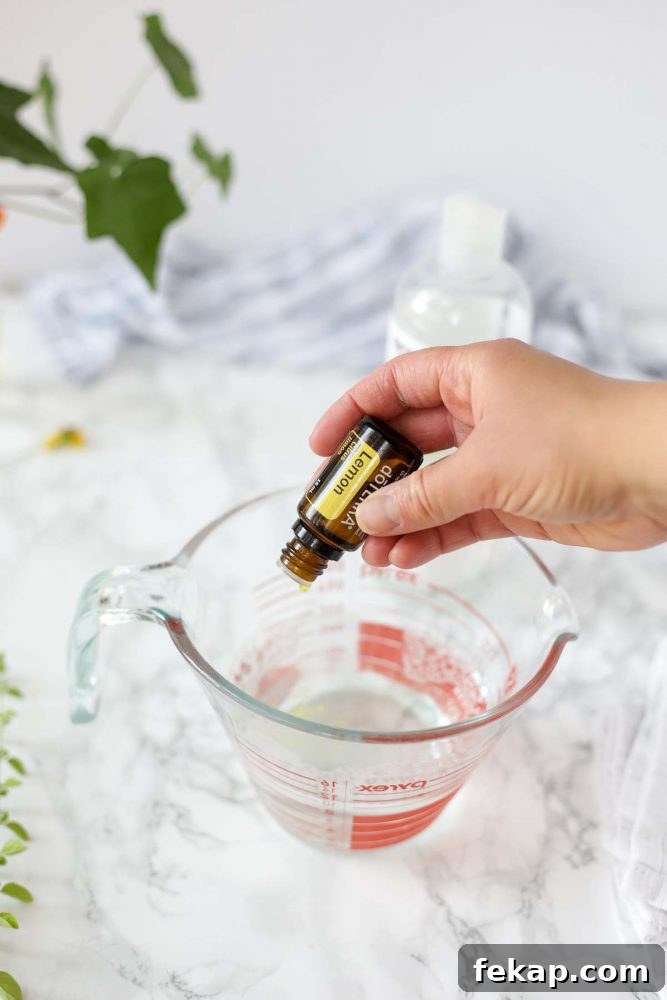 DIY Natural Dish Soap Recipe That Cuts Grease 7 adding lemon essential oils to a homemade dish soap in a glass measuring cup