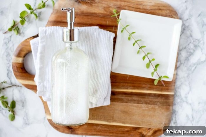 DIY Natural Dish Soap Recipe That Cuts Grease 8 natural soap in a glass jar on a white dish cloth on a wood cutting board with a white plate to the right