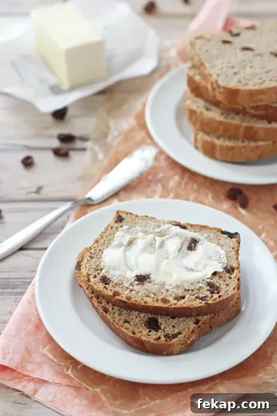 Whole wheat cinnamon raisin bread with one rise and a soft, toastable crumb. Two slices of whole wheat cinnamon raisin bread on a plate with one slice buttered.