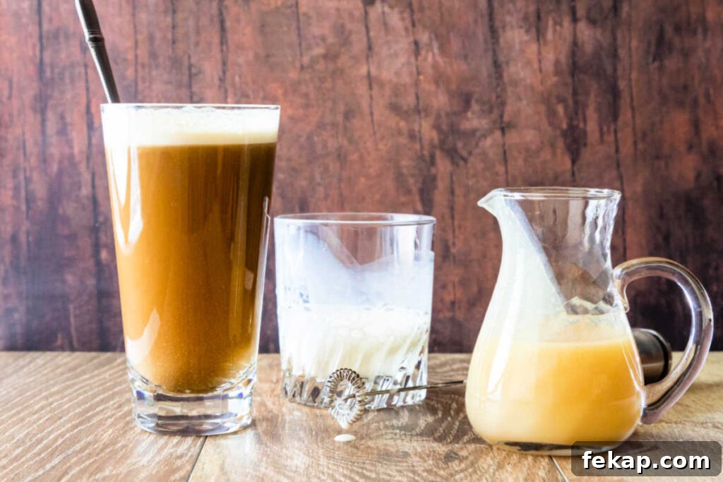 How to Make Silky White Chocolate Sauce 4 A glass containing white chocolate mocha, a glass with foamed milk in it, and a small glass pitcher of white chocolate syrup.