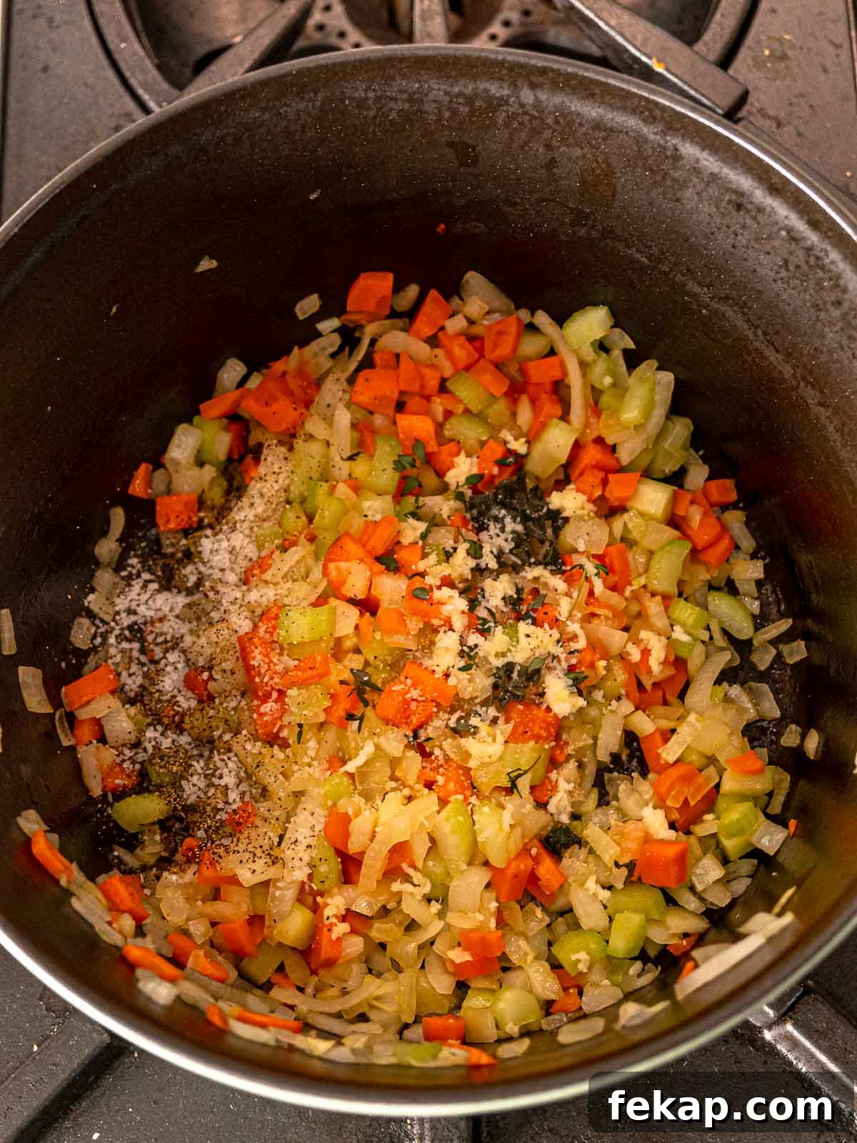 Sautéed vegetables in a pot topped with garlic, herbs, salt, and pepper.