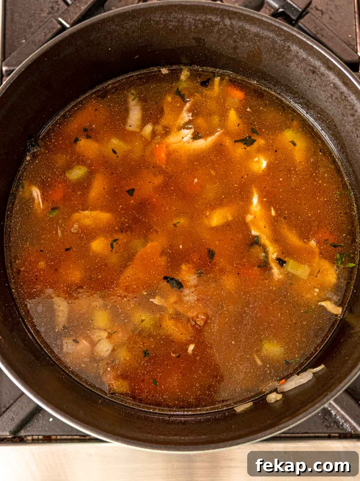 Dutch oven with turkey broth, vegetables, and shredded turkey simmering for soup.