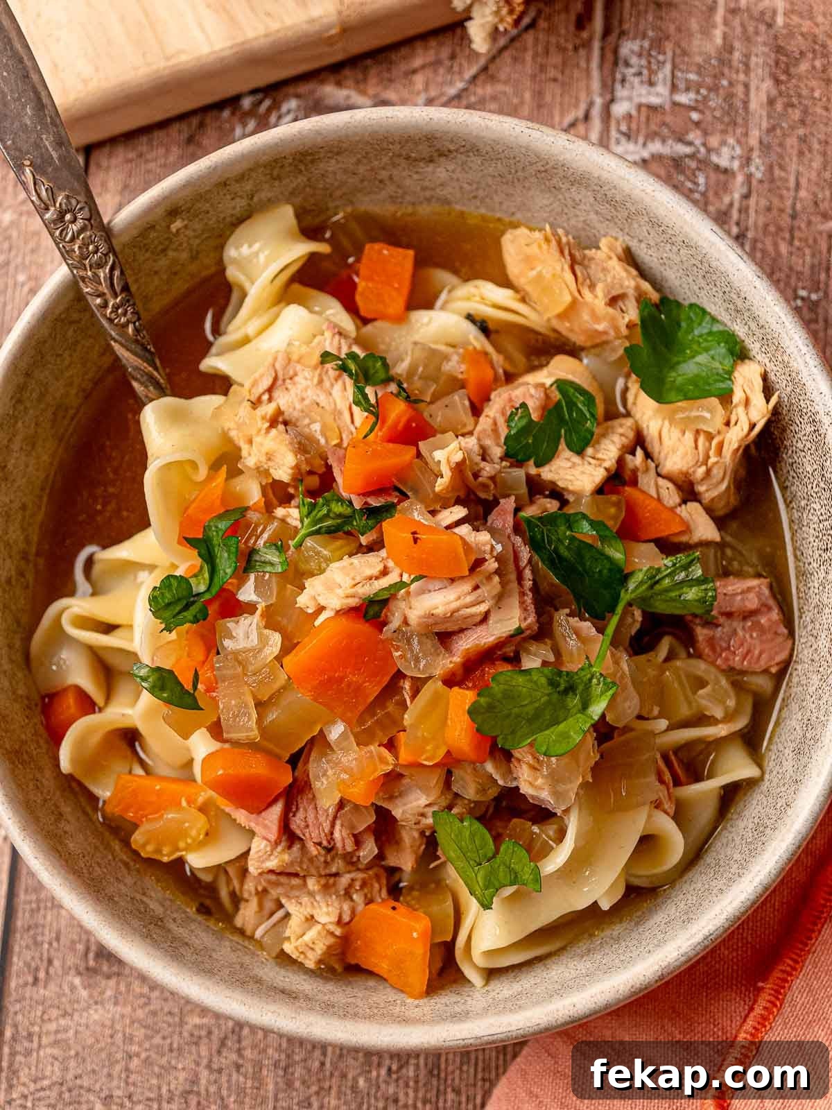 Leftover turkey noodle soup in a bowl garnished with parsley, showing noodles and veggies.