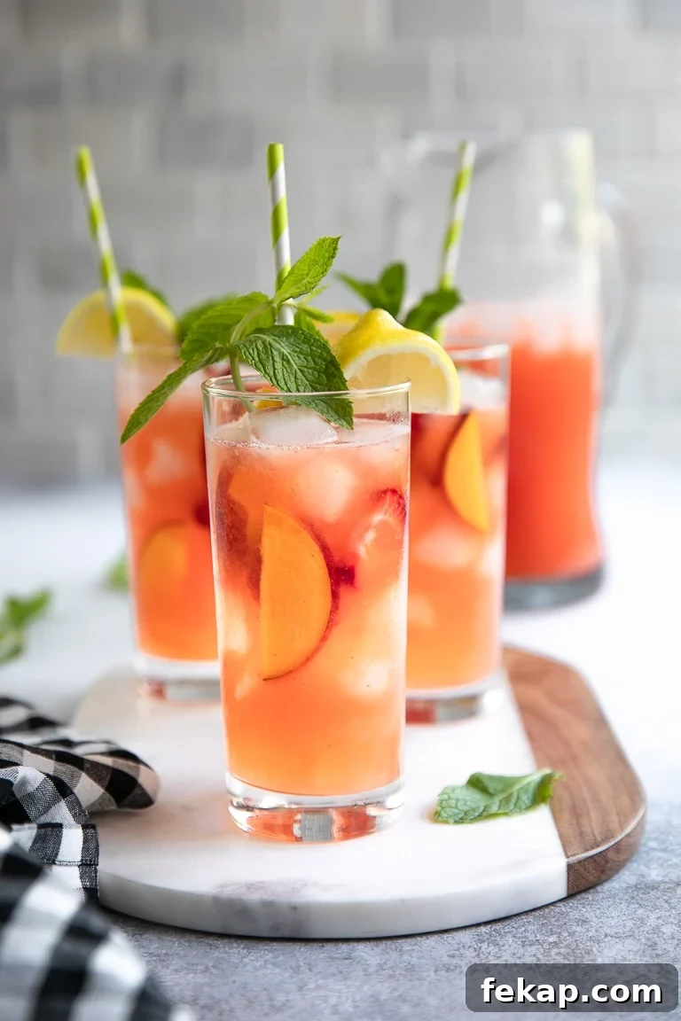 Refreshing Peach Strawberry Lemonade Recipe for Summer 2 Tall glasses filled with peach and strawberry lemonade garnished with fresh mint.