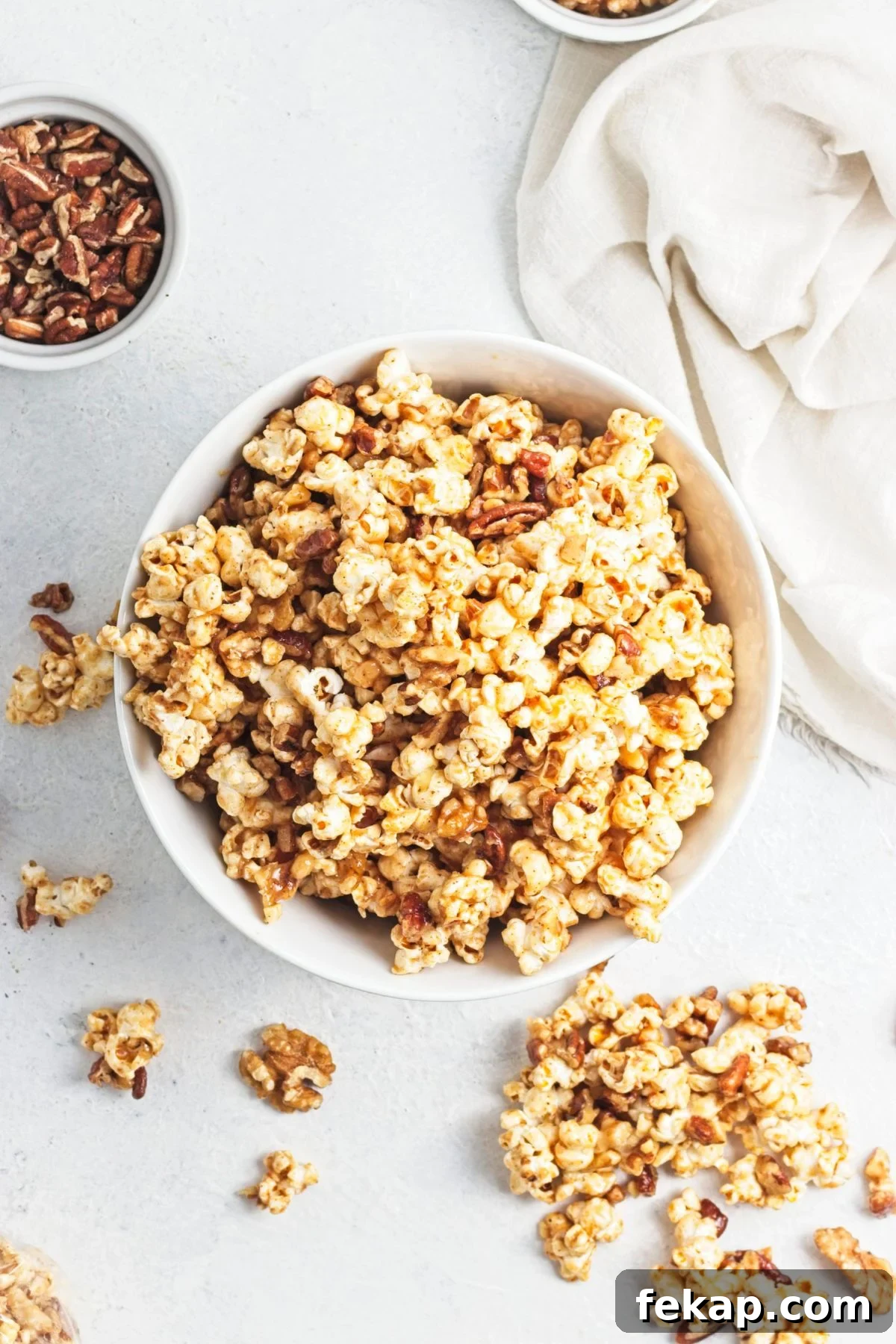 A white bowl filled with caramel popcorn and more popcorn in front of the bowl.