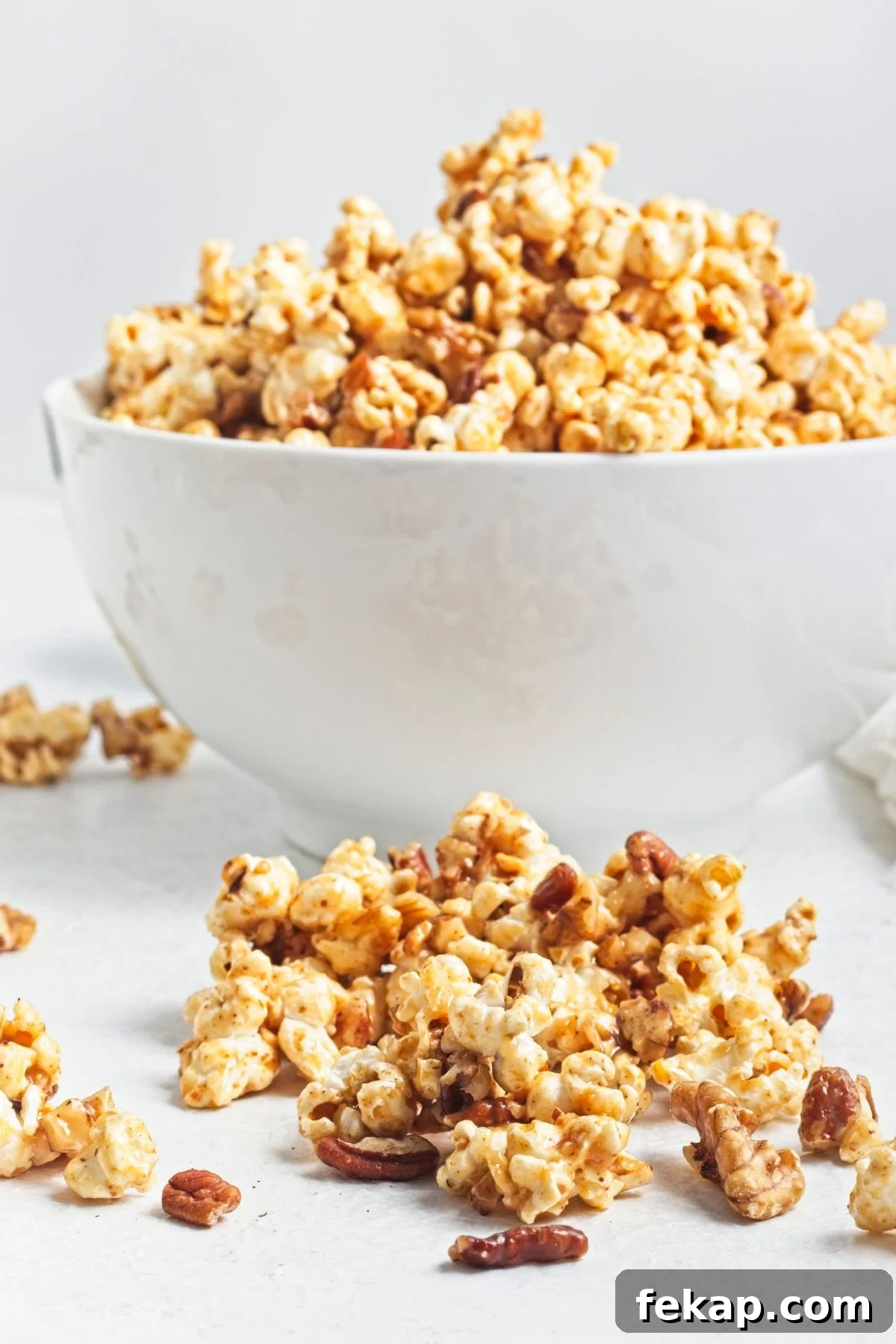 A white bowl filled with caramel popcorn and more popcorn in front of the bowl.