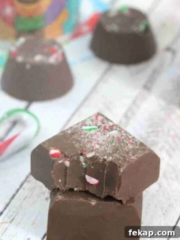 Two pieced of candycane fudge stacked the top with a bite out of it and more fudge and candy canes behind them.