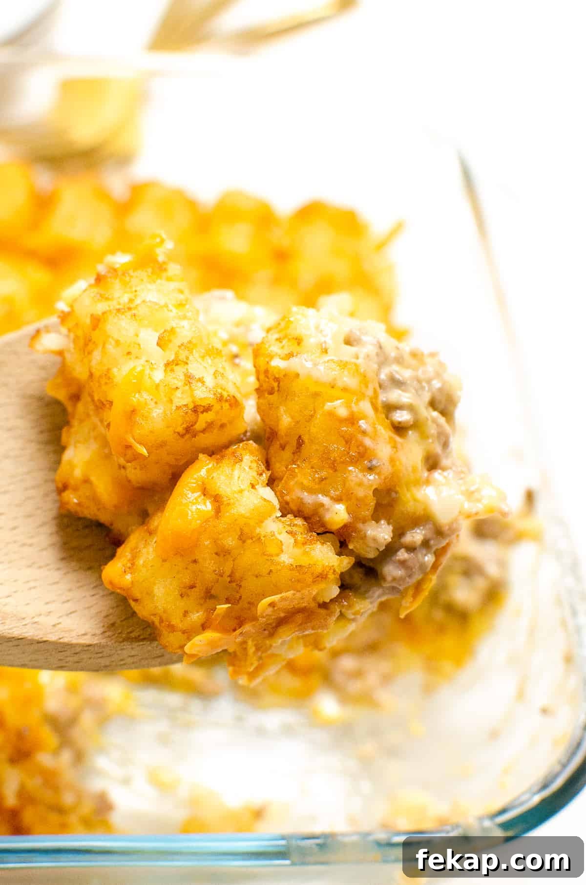 Wooden spoon full of tater tot casserole with ground beef and cheese