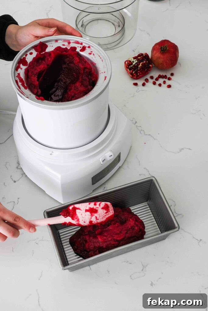 Homemade Pomegranate Sorbet Recipe 12 A spatula scoops pomegranate sorbet out of an ice cream maker and into a chilled loaf tin.