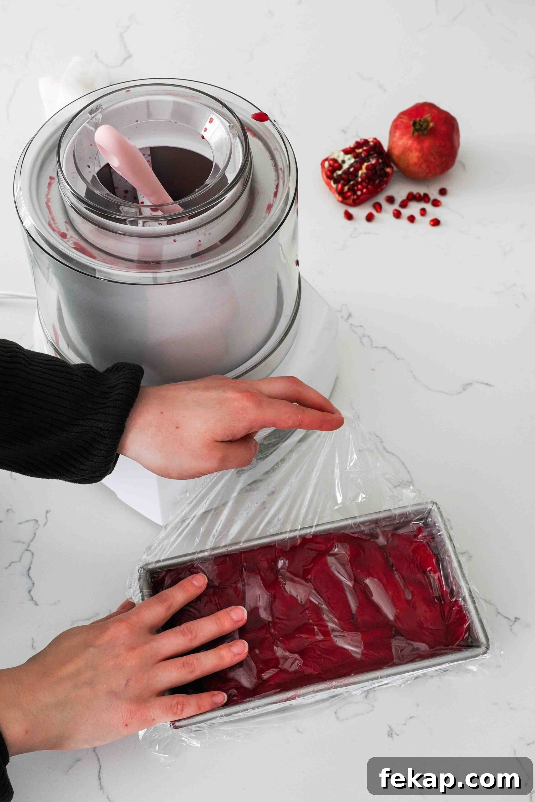 Homemade Pomegranate Sorbet Recipe 13 Two hands place plastic wrap over a loaf tin filled with pomegranate sorbet.