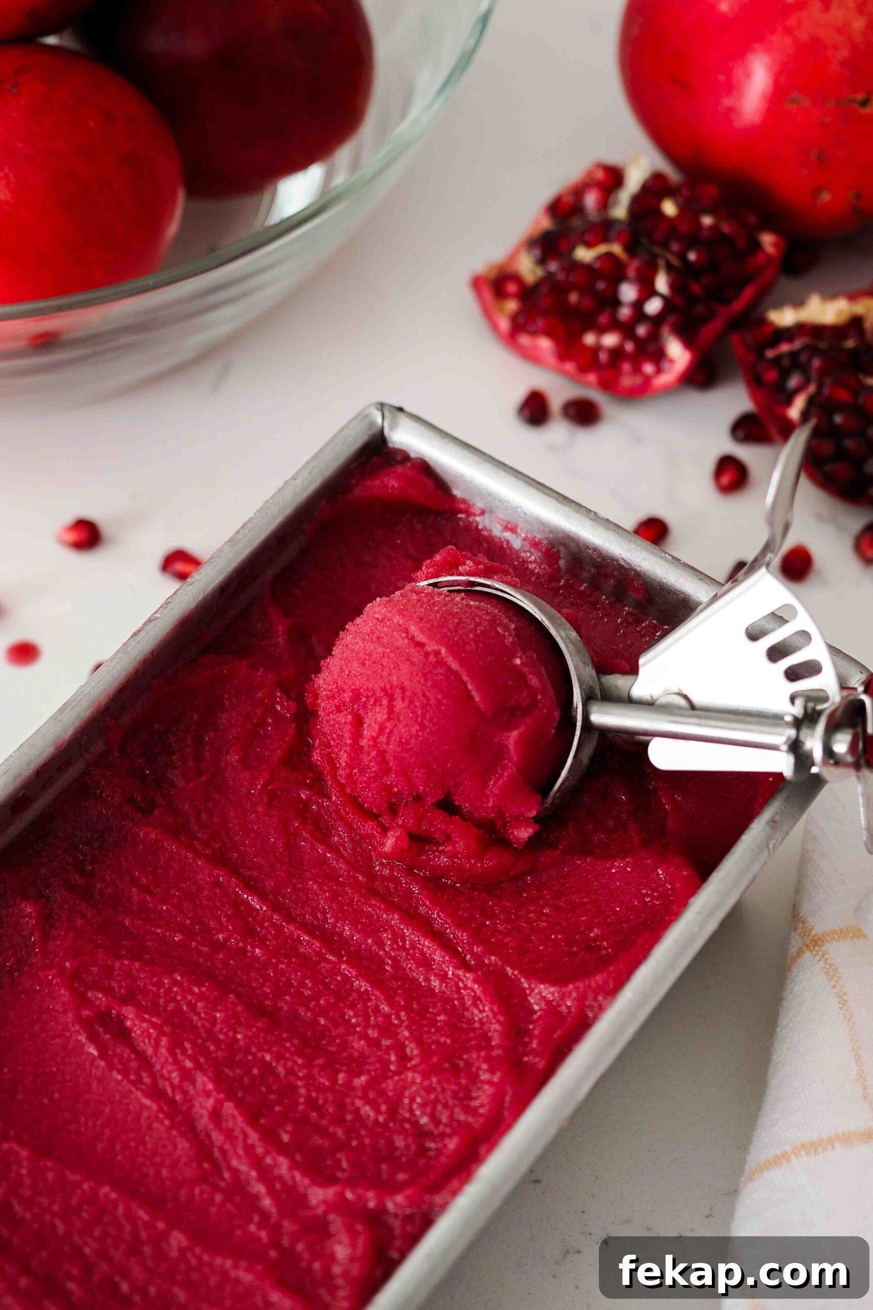 Homemade Pomegranate Sorbet Recipe 14 An ice cream scoop filled with pomegranate sorbet over a loaf tin of sorbet.