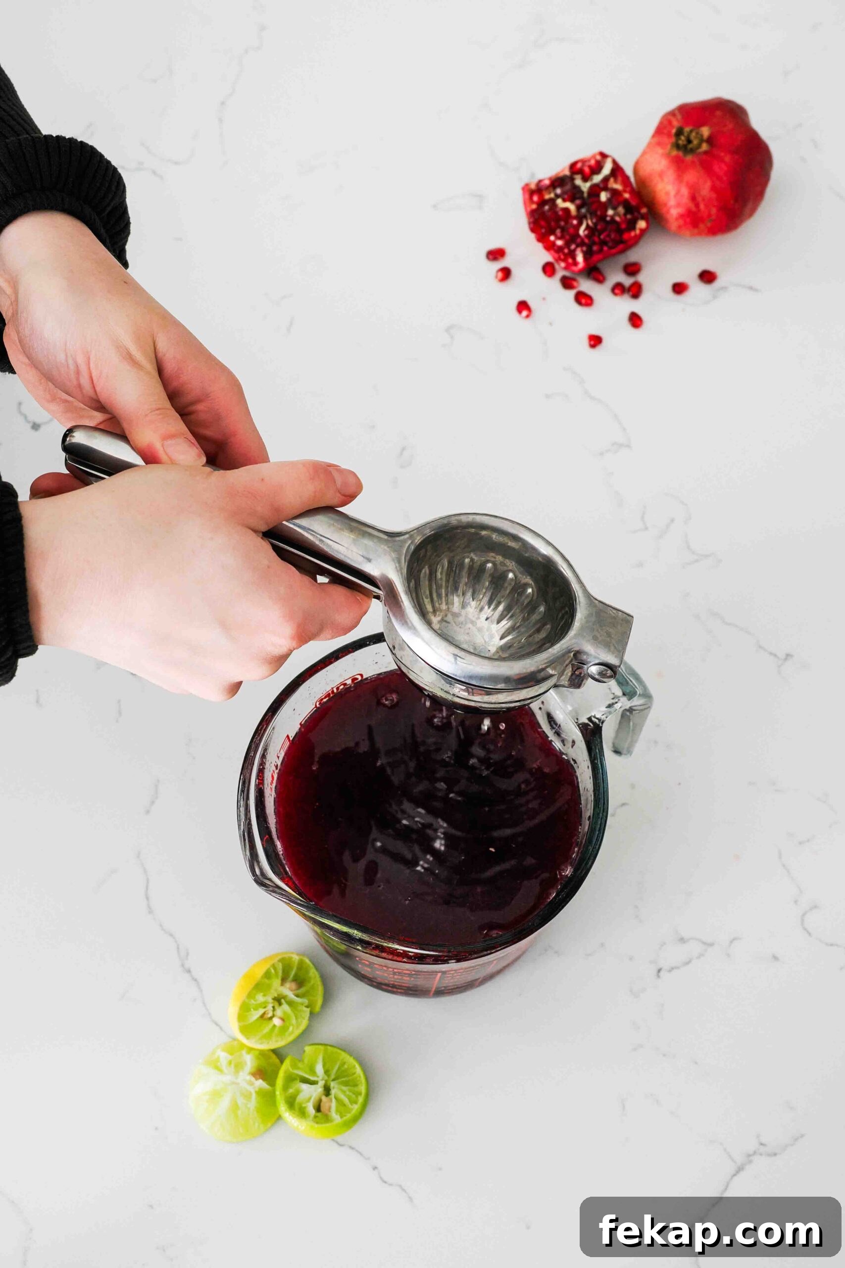 Homemade Pomegranate Sorbet Recipe 5 Two hands squeeze lime juice into a measuring cup.