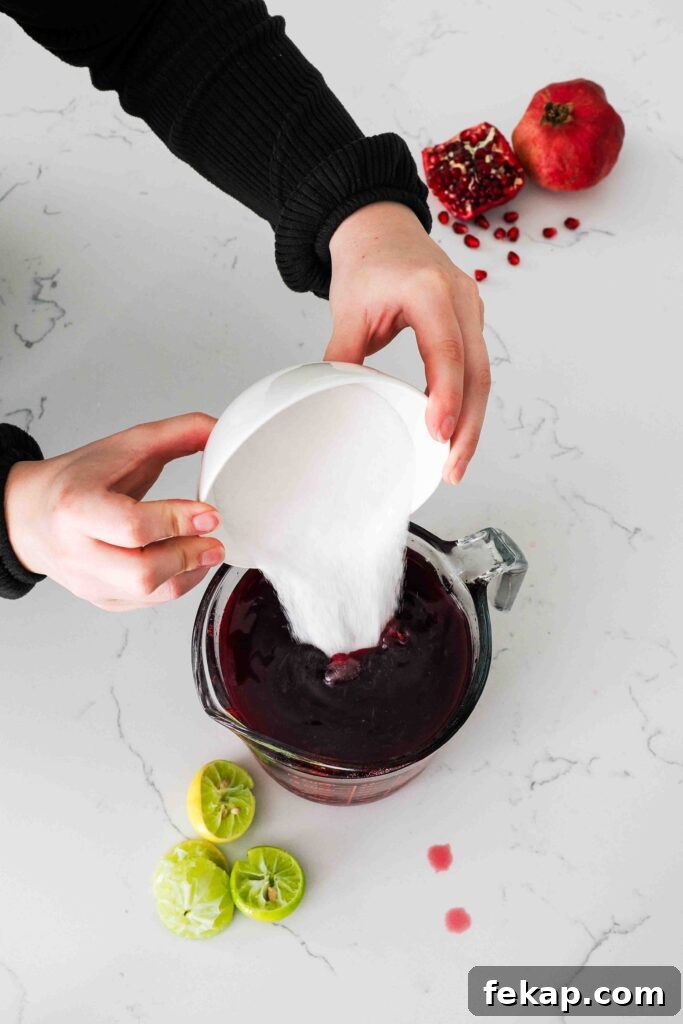Homemade Pomegranate Sorbet Recipe 6 Two hands pour sugar into a pomegranate juice-filled measuring cup.