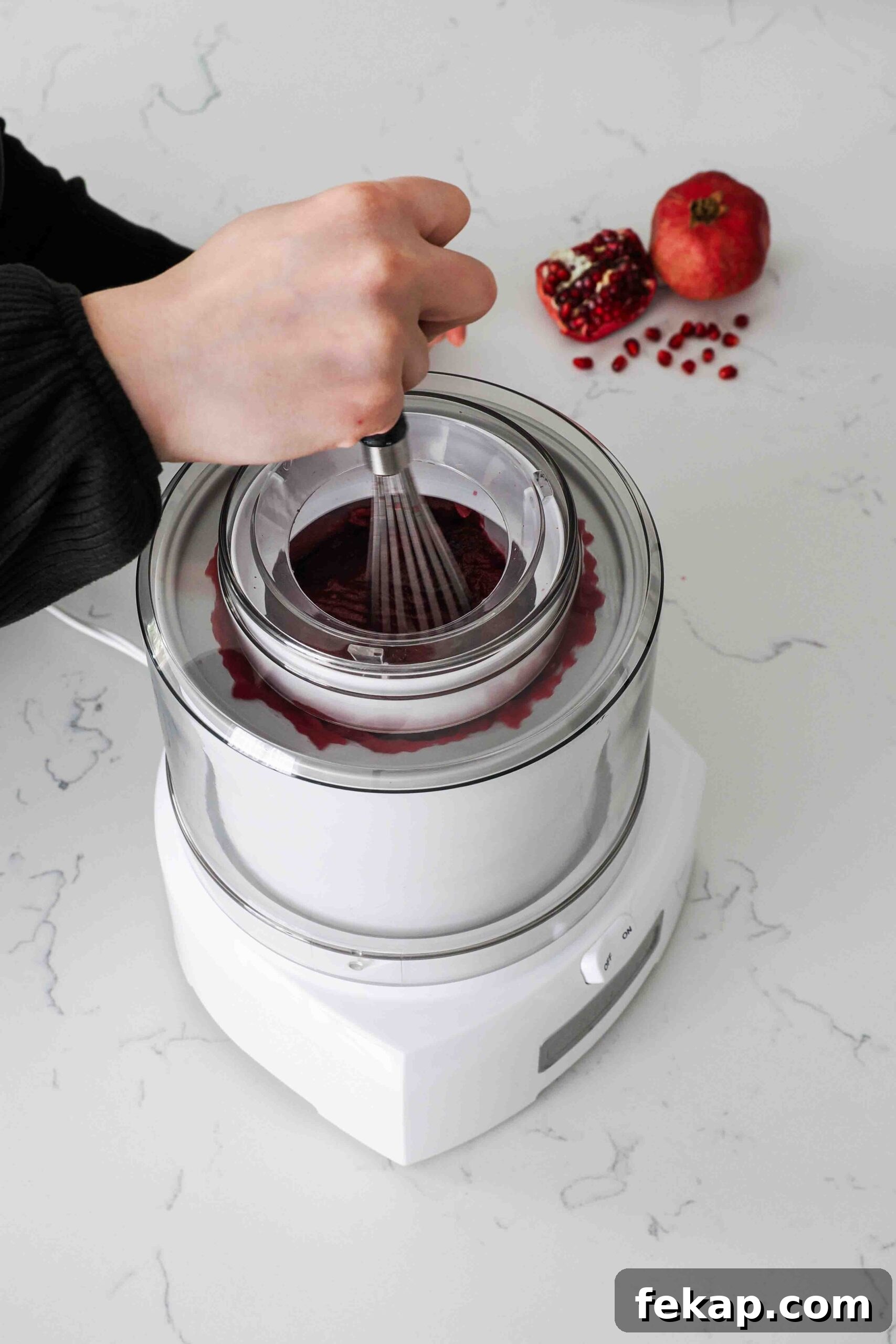 Homemade Pomegranate Sorbet Recipe 10 A hand uses a whisk to break up frozen chunks of pomegranate sorbet in an ice cream maker.