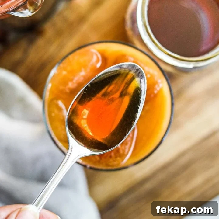 Homemade caramel syrup for coffee on a spoon with a glass of iced coffee.