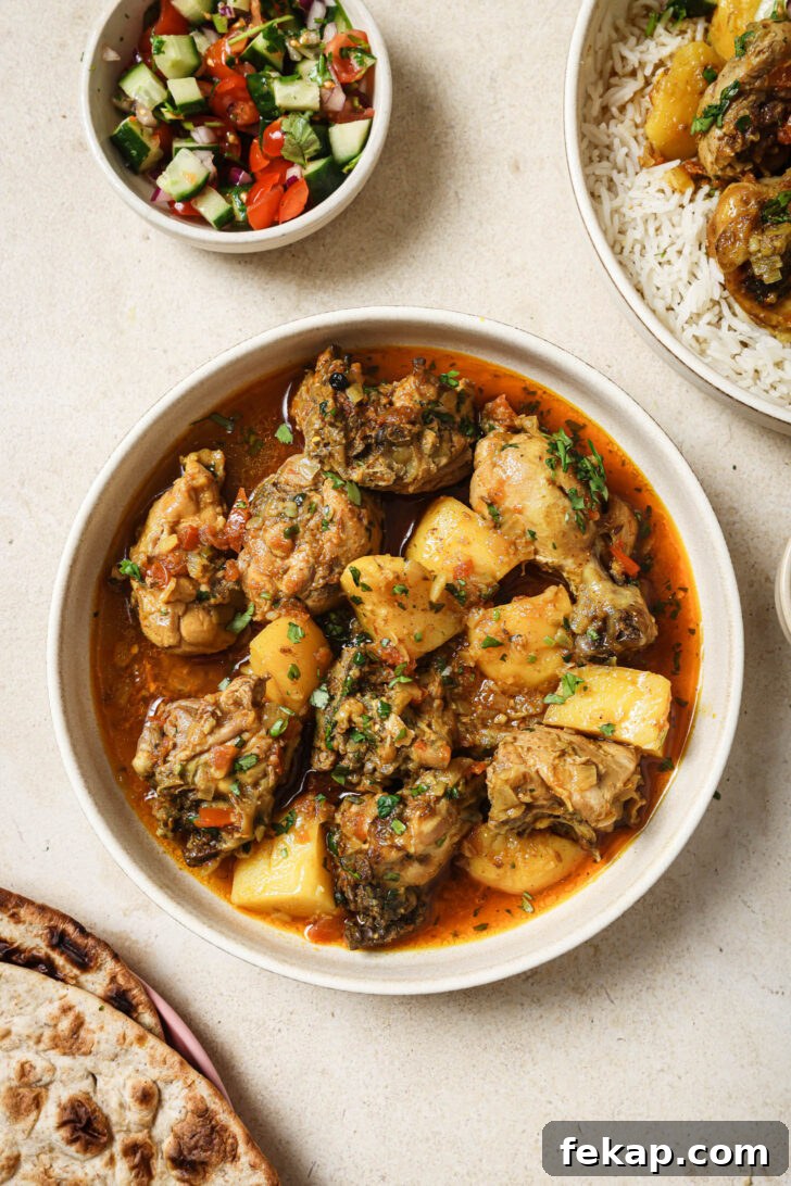 Pakistani Chicken Curry in a bowl surrounded by bowl of Kachumber, naan and a bowl iwth rice topped with Chicken Curry.