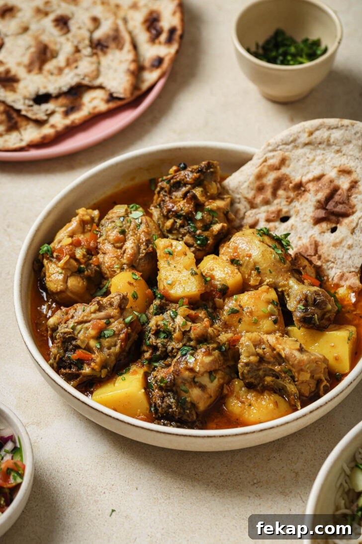Close up of a bowl of Pakistani Chicken Curry garnished with cilantro and garam masala with a piece of naan on the side.