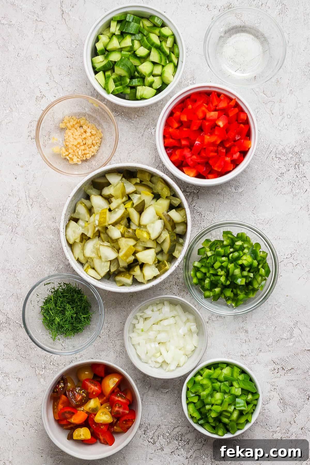 Individual bowls of sliced and quartered cucumber, diced bell pepper, minced garlic, sliced and quartered pickles, fresh dill, diced white onion, quartered cherry tomatoes, diced green bell pepper, diced anaheim pepper, and pickle brine. 