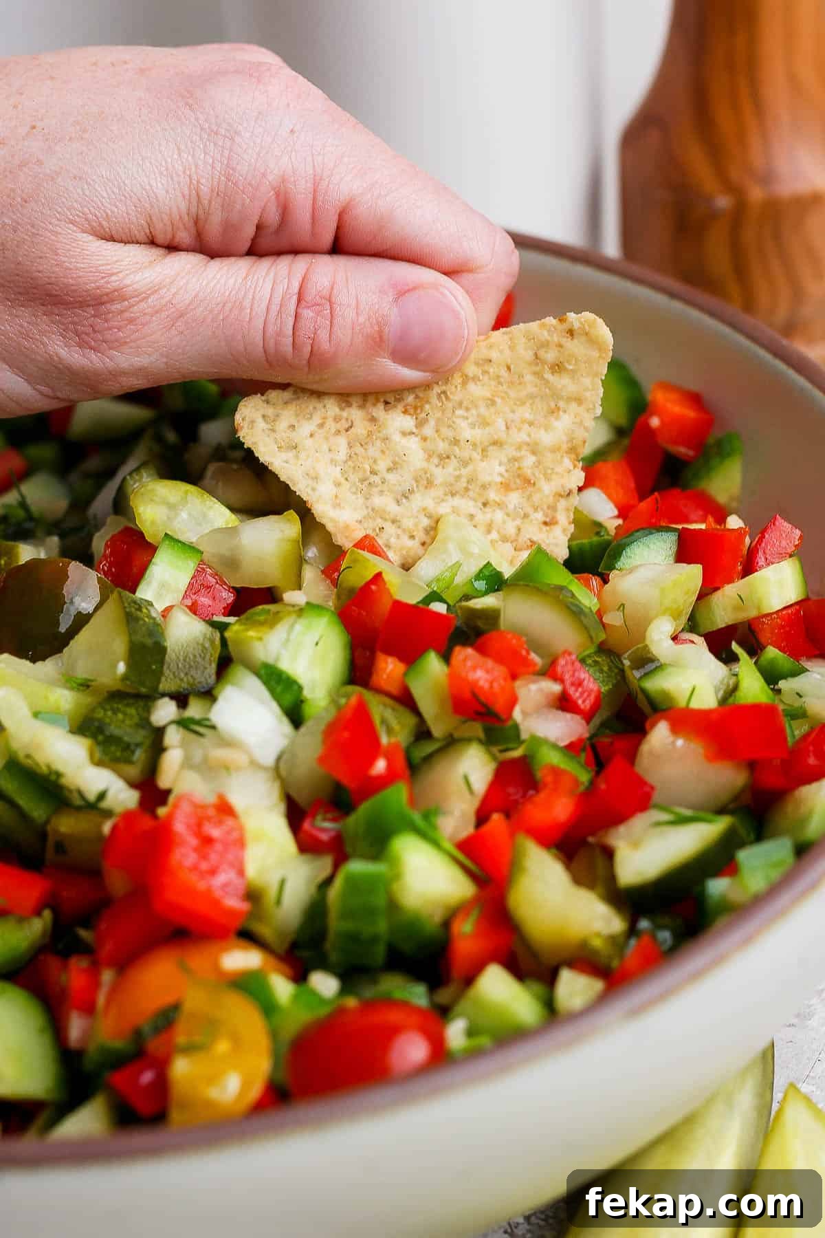 A hand holding a chip and dipping it into the pickle de gallo.